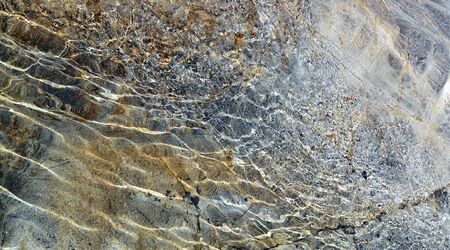 Colored rock is seen through the clear water with waves and sunlight spots.