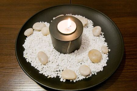 Candle in a wooden candlestick on a wooden plate, in the Chinese style. Pebbles are around scattered.の写真素材