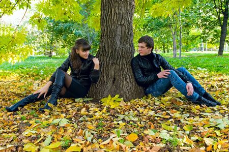 The enamoured sit on leaves in autumn parkの写真素材