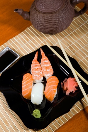 Tasty dish of assorted sushi on black plate and teapotの写真素材
