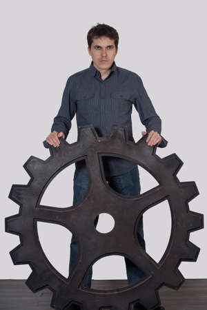 Young man holding a large gear, on a gray backgroundの写真素材