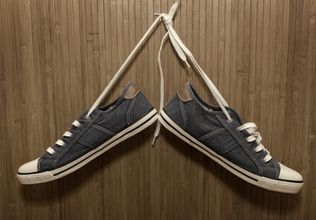 New, denim sneakers hanging on a bamboo wallの写真素材