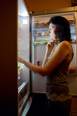 Woman in pajamas at night chooses the food in the fridgeの写真素材