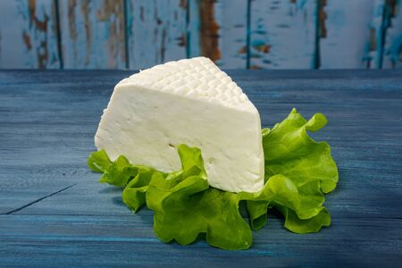 Piece of cheese on a leaf of green salad lies on a blue wooden tableの写真素材