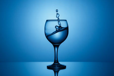 Splash of clear water in a glass on a blue backgroundの写真素材