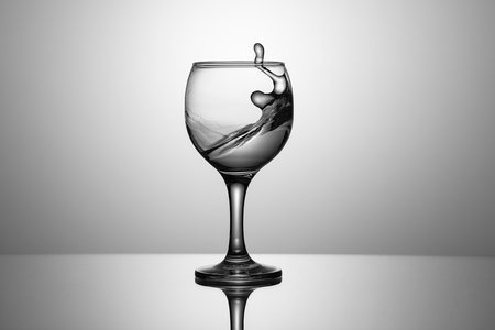 Splash of clear water in a glass on a glass background with reflectionの写真素材