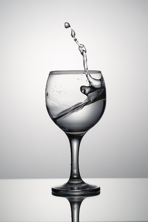 Splash of clear water in a glass on a glass background with reflectionの写真素材