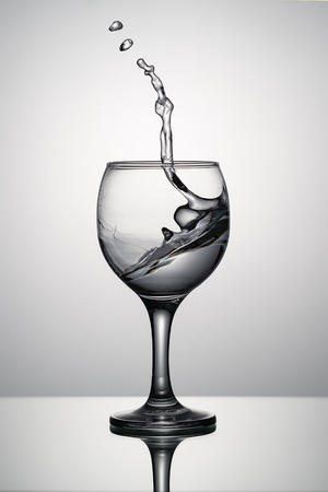 Splash of clear water in a glass on a glass background with reflectionの写真素材