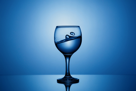 Splash of clear water in a glass on a blue backgroundの写真素材