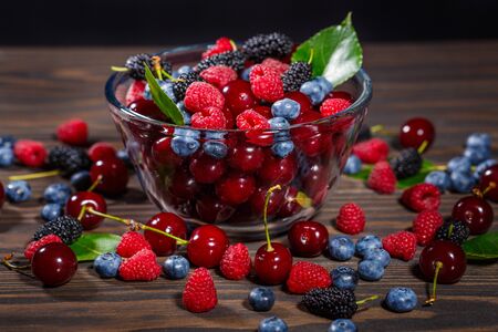 Summer, ripe berries in a transparent bowl on a dark wooden backgroundの写真素材