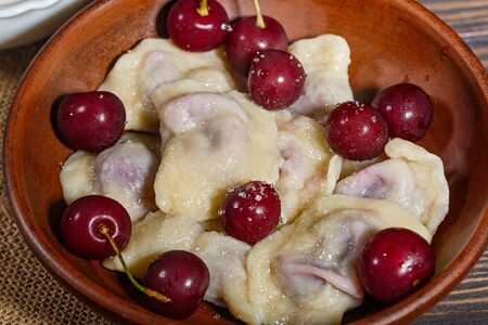 Clay bowl of dumplings with cherries on a napkin with burlapの写真素材