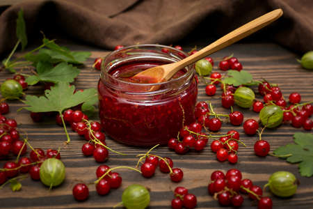 Jam and red currant berries on a dark, wooden background