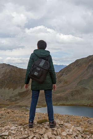 Woman with a backpack stands on the edge of a cliff above a mountain lakeの写真素材