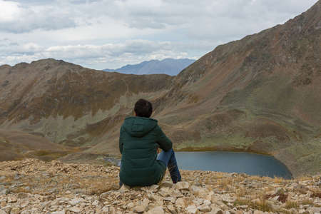 Woman traveler sits on the edge of a cliff above a mountain lakeの写真素材