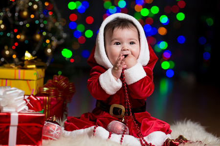 kid girl dressed as Santa Claus near Christmas tree with giftsの写真素材