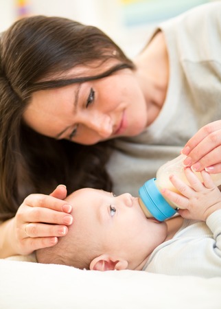 mother feeding baby son with a milk bottle at homeの写真素材