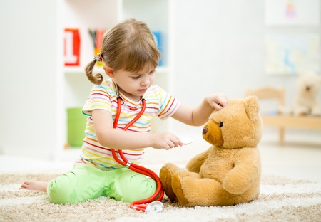 child girl playing doctor and curing plush toy indoorsの写真素材