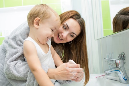 Happy mother and kid wash hands with soap in bathroomの写真素材