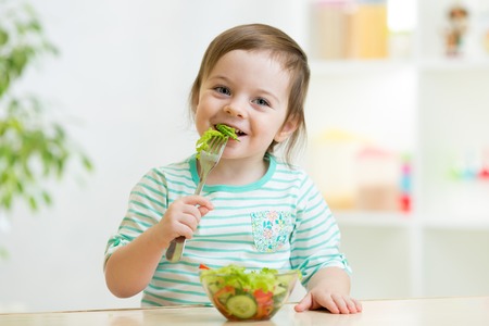 kid girl eating healthy vegetables at kitchenの写真素材