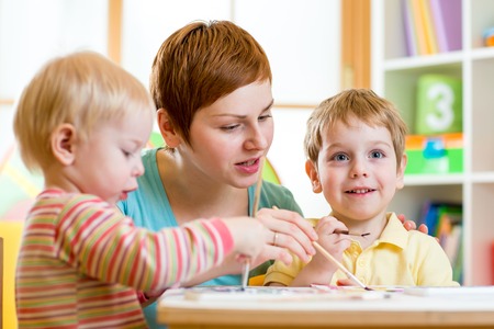 cute woman teaching kids to paint at nursery or playschoolの写真素材