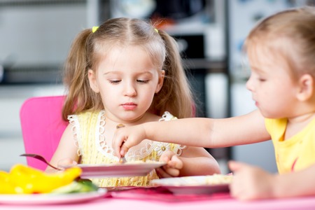 children eating spaghetti with vegetables in nursery or at homeの写真素材