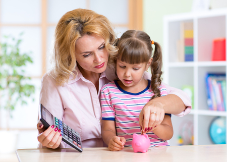family - middle aged mother and kid daughter with pink piggy bank and calculatorの写真素材