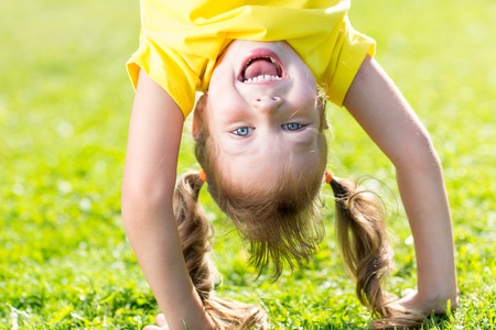 Happy child girl has a fun standing head down on green grassの写真素材