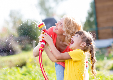 Happy woman and kid daughter watering in domestic garden at summer dayの写真素材