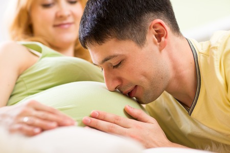 Future dad embracing and kissing belly of his pregnant wife