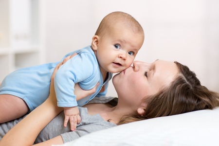 Cute mother kissing baby lying on bed in nurseryの写真素材