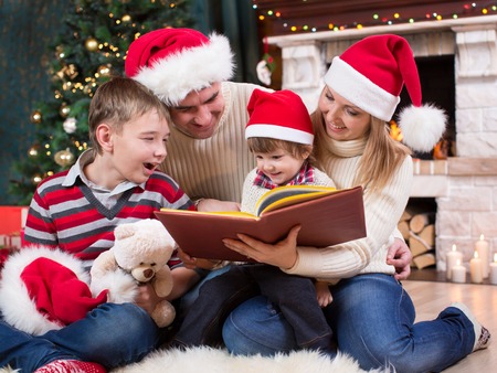 Family reading a book together in front of Christmas treeの写真素材