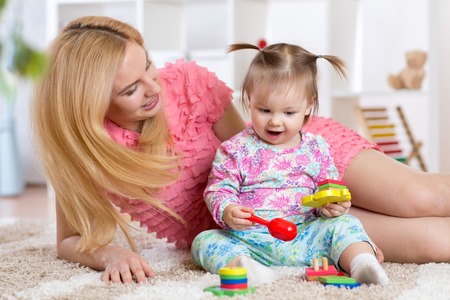 Cute baby playing with her mother on carpet in nurseryの写真素材