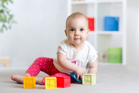 beautiful baby girl plays cubes on the floor and smiling