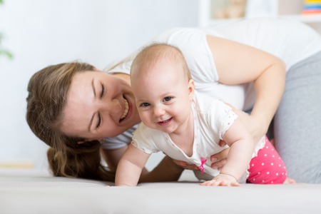 Funny crawling baby girl with mother on bed at homeの写真素材