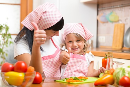 Happy mother and daughter with fresh vegetables showing thumbs up gesture. Shot in the kitchenの写真素材