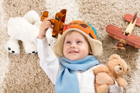 Happy kid boy playing with toy airplane lying on floorの写真素材