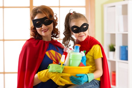 Cute child girl and her mother make cleaning the house. Little girl and mom are dressed in superman costumes.の写真素材