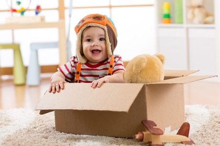 Smiling pilot aviator baby boy with teddy bear toy plays in cardboard boxの写真素材