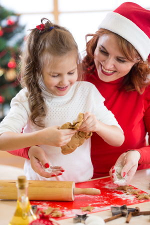 Child girl with her mother baking Christmas cookies in the kitchenの写真素材