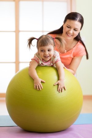 Mother with happy child doing exercises with gymnastic ball at fitness class. Concept of caring for the babys health.の写真素材