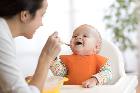 Mother feeding her baby with spoon. Mother giving healthy food to her adorable child at homeの写真素材