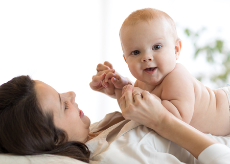 Mother and baby hugging and playing lying indoorsの写真素材