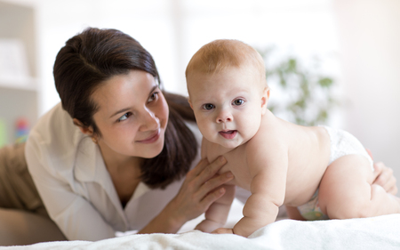 Mom and her little son weared diaper on bed. Mother embracing infant baby.の写真素材