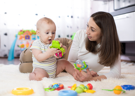 Funny baby and young woman playing in nursery. Happy family having fun with colorful toys at home.の写真素材