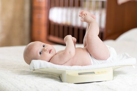 Cute little baby girl lying on scales at homeの写真素材