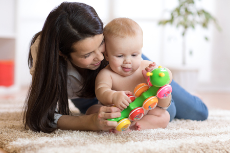 Mother and her baby son play with toy in cosy children roomの写真素材