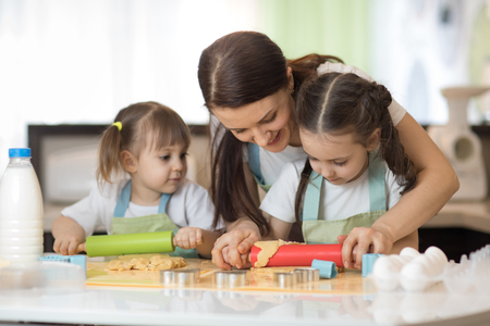 Cute little kids and their beautiful mom in aprons are playing and laughing while kneading the dough in the kitchenの写真素材