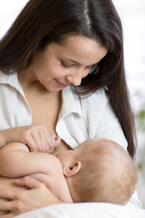 Young mother holding her newborn child. Mom nursing baby. Pretty woman breast feeding kid.の写真素材