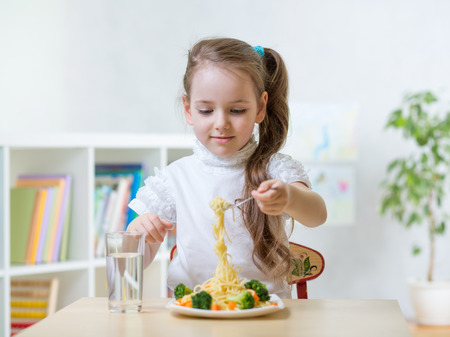 Kid little girl eats vegetarian food at home or kindergartenの写真素材
