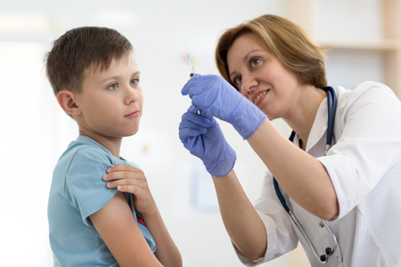 Doctor holds syringe and teenager patient. Little brave boy before injection.の写真素材